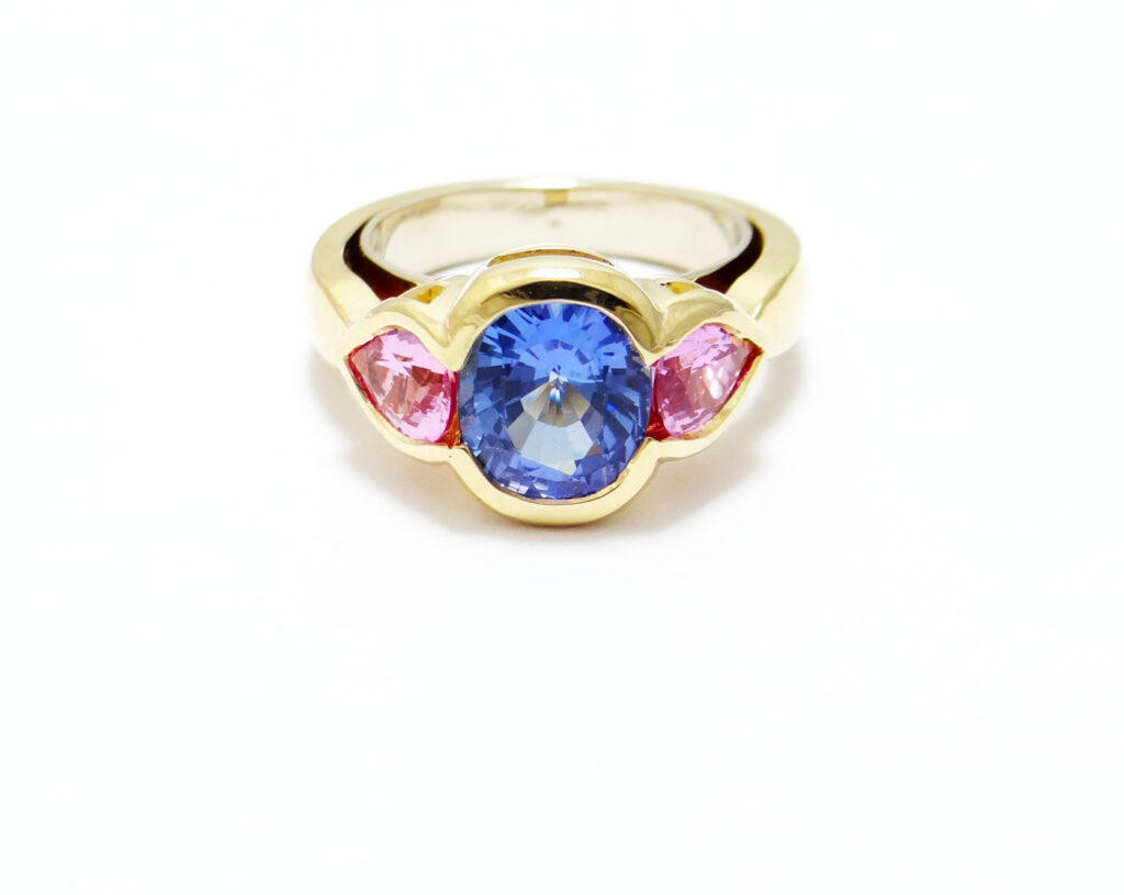 bague moderne avec une tanzanite au centre taille coussin de 3 carats et deux saphirs rose poire sur les cotés monture or jaune